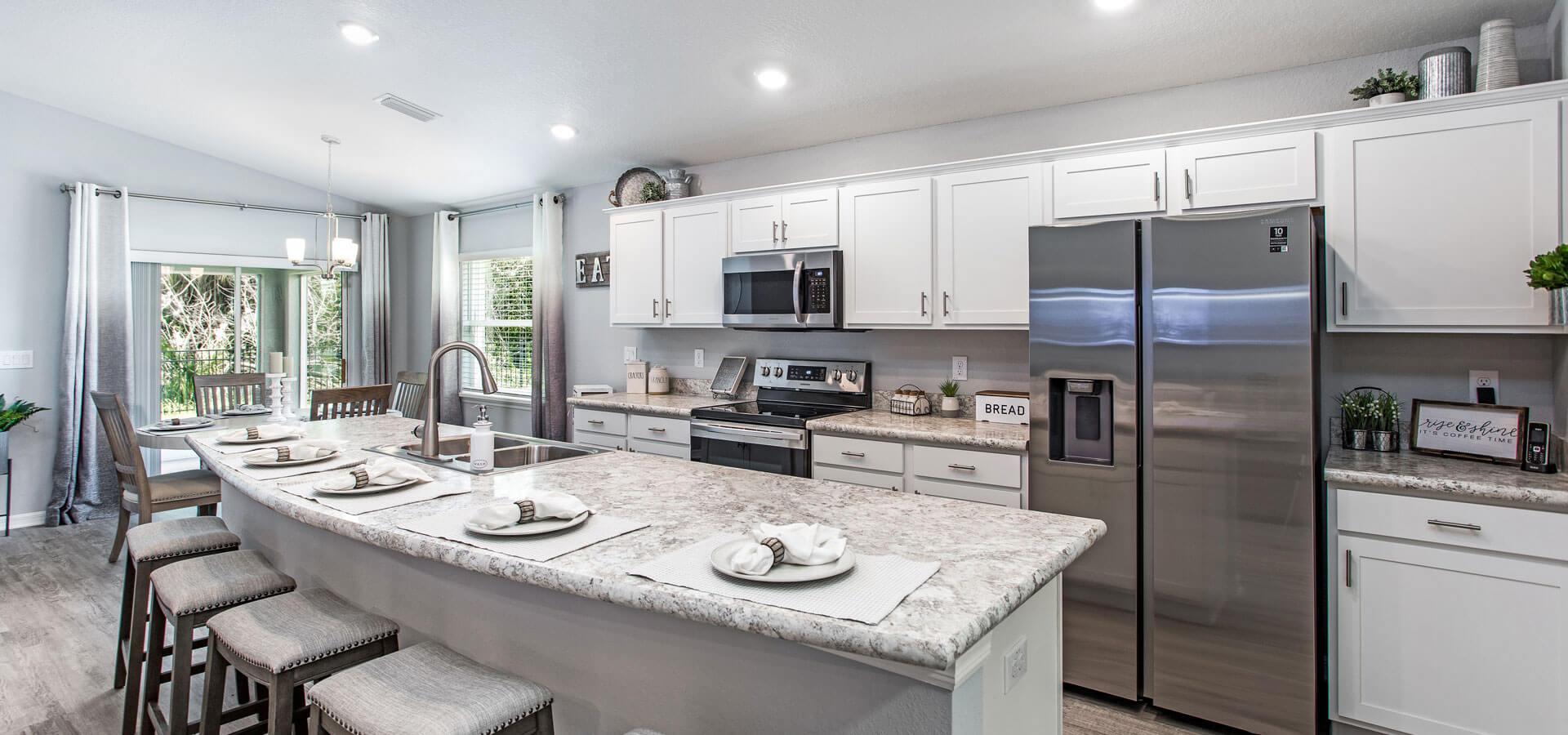 Open kitchen with white cabinets and stainless steel appliances in the Raychel, a new home plan by Highland Homes